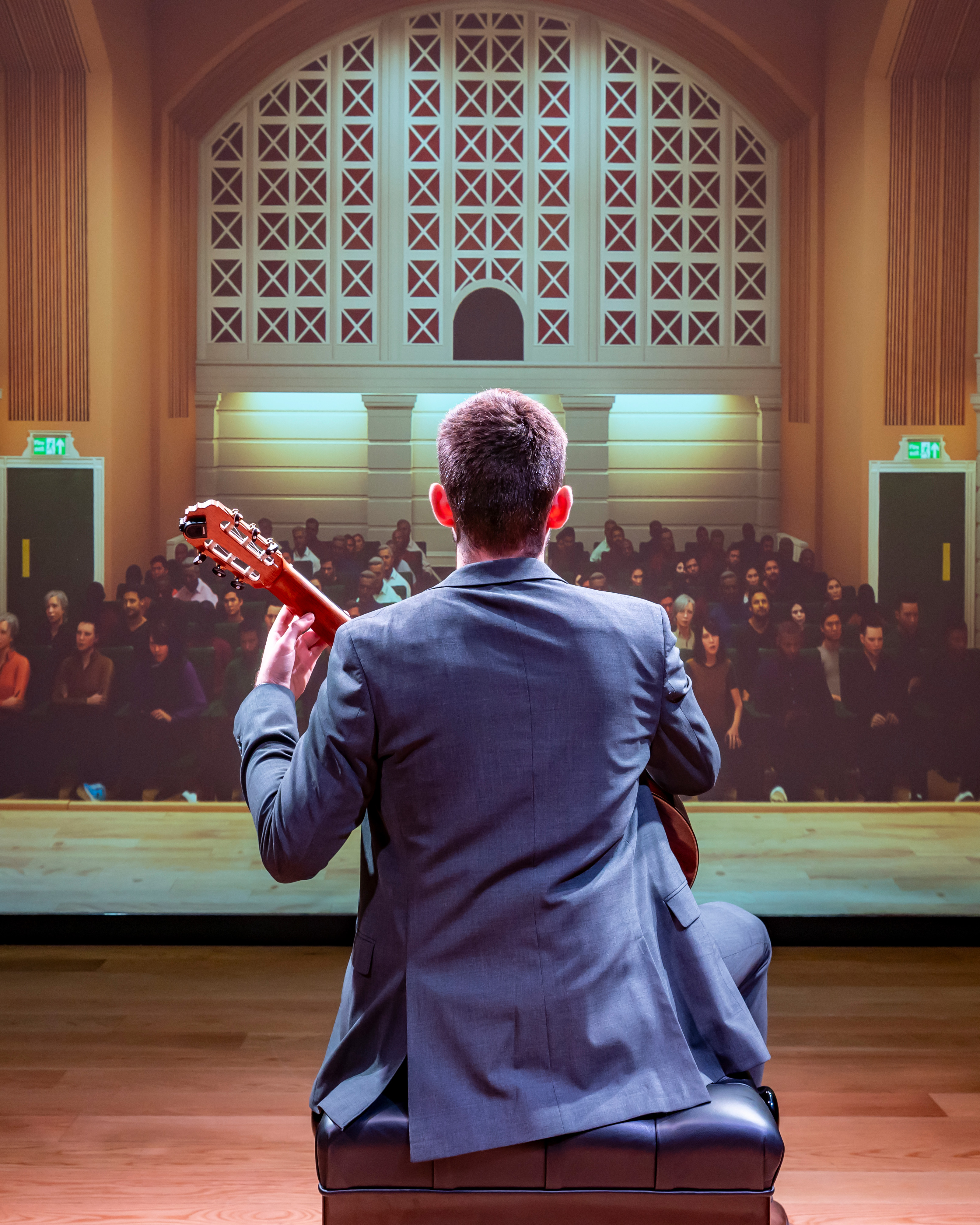 A male guitar student, wearing a smart suit, performing to a virtual audience.